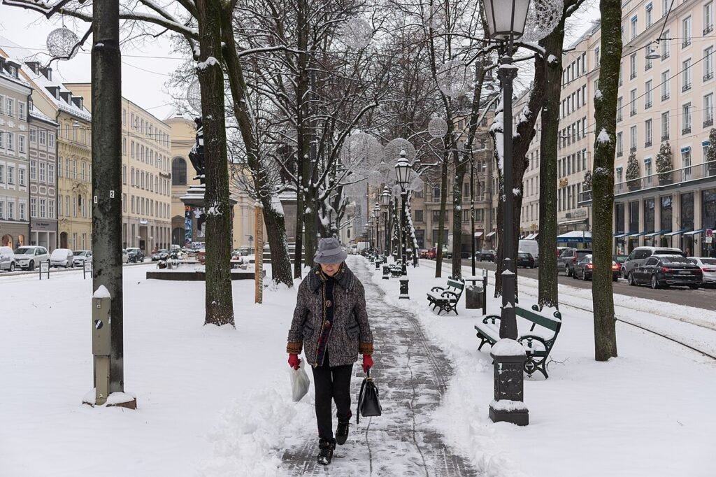 Older woman in a winter coat walking alone along a snow-covered path